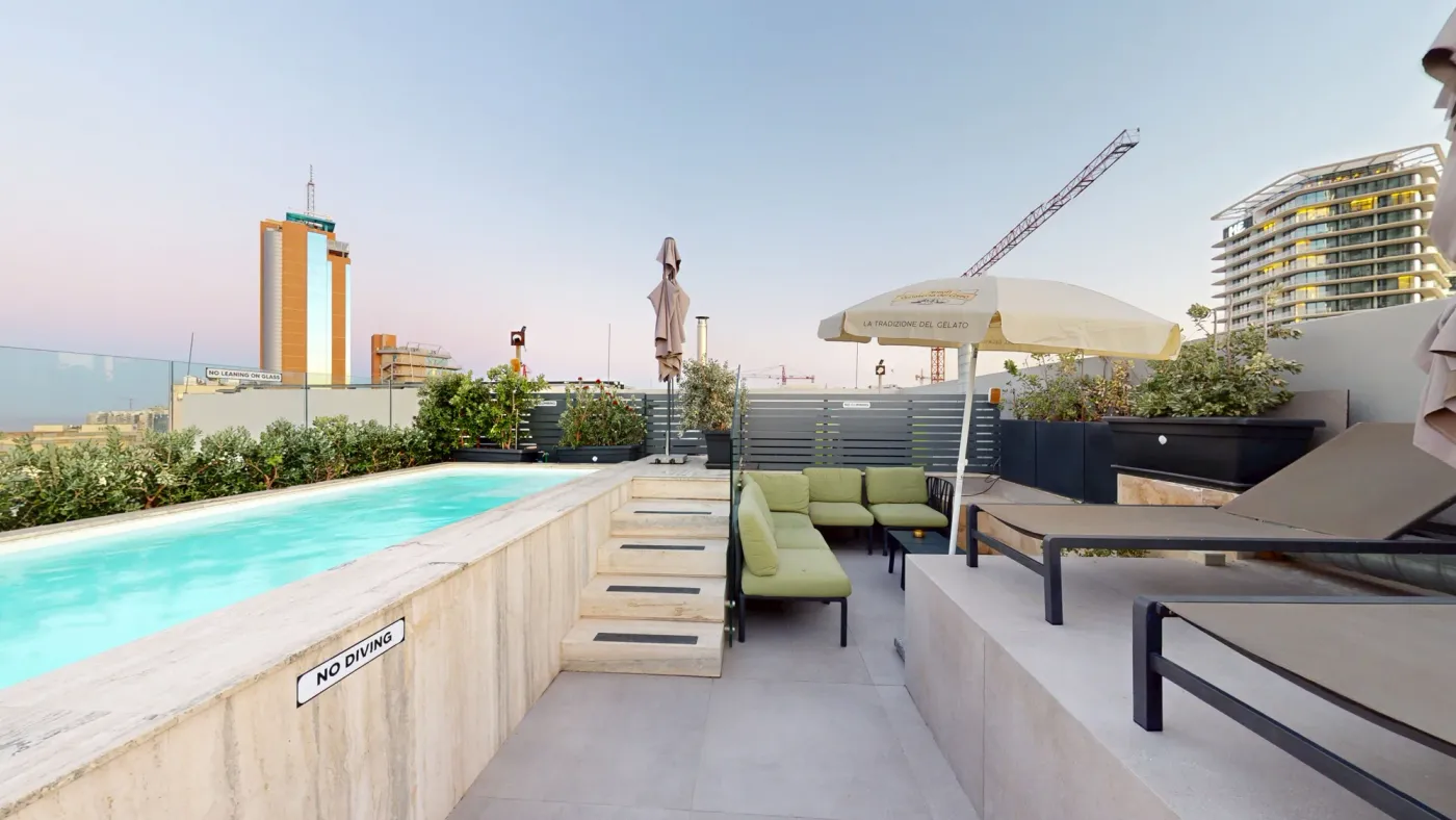 Hotel rooftop with a pool and views of the Malta skyline at sunset