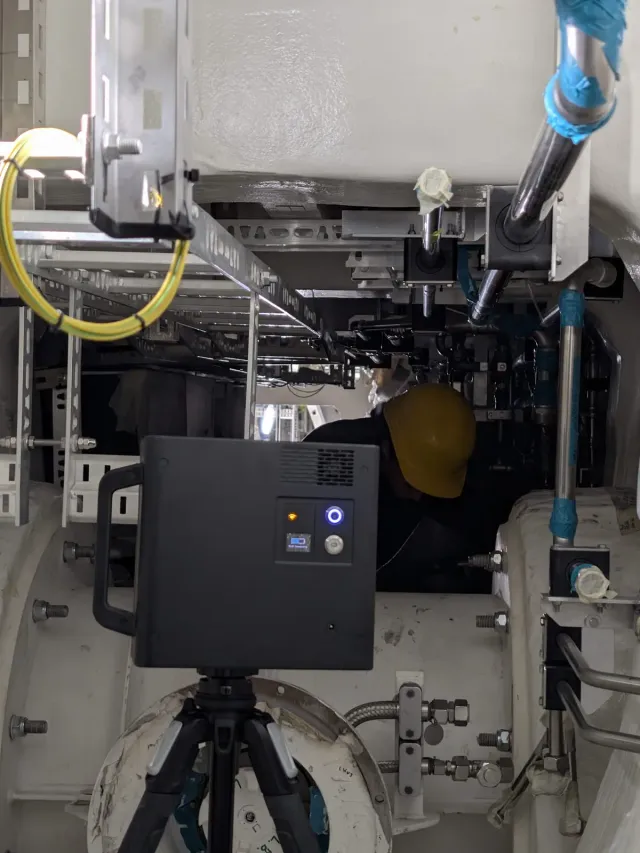 3D camera scanning the interior of a superyacht under construction, with a worker in a hard hat in the background